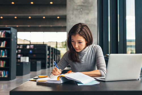 Female,Student,Taking,Notes,From,A,Book,At,Library.,Young